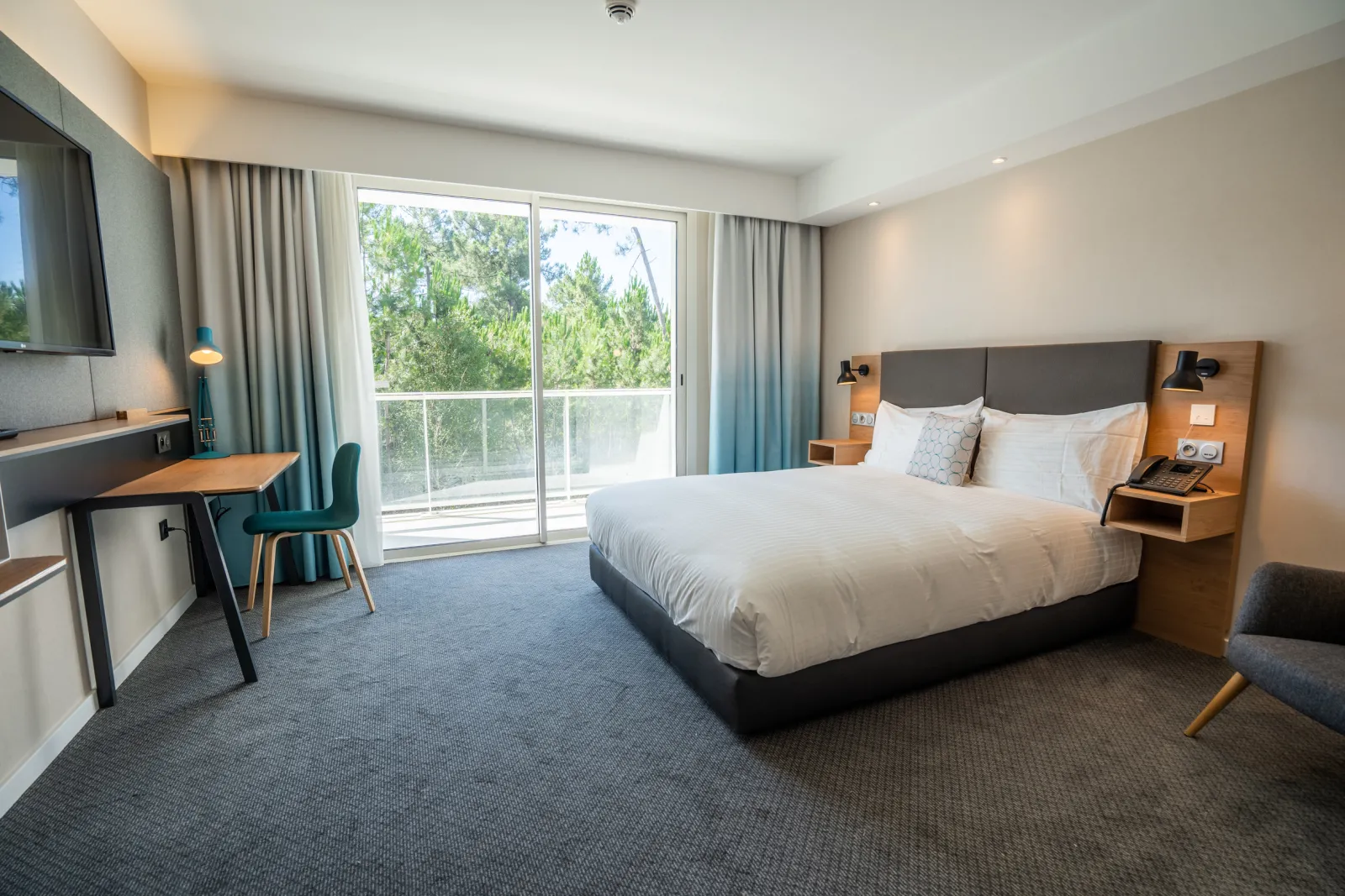 Chambre d'hôtel moderne avec lit king-size, bureau, télévision, et large baie vitrée donnant sur des arbres, au Holiday Inn Bordeaux Mérignac