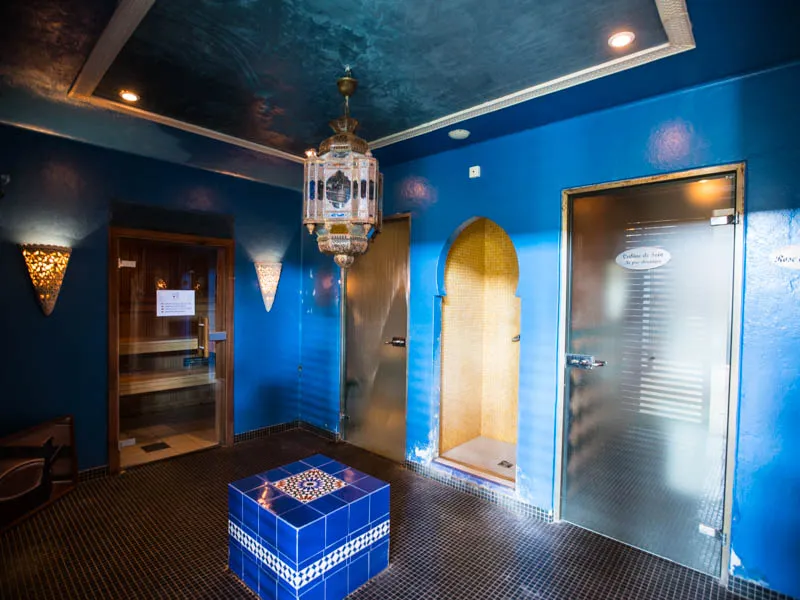 Espace spa marocain aux murs bleu profond avec plafond étoilé, luminaire suspendu doré, deux portes vitrées et un bassin carrelé bleu et blanc au centre, chez Les Bains de Margaux à Bordeaux.