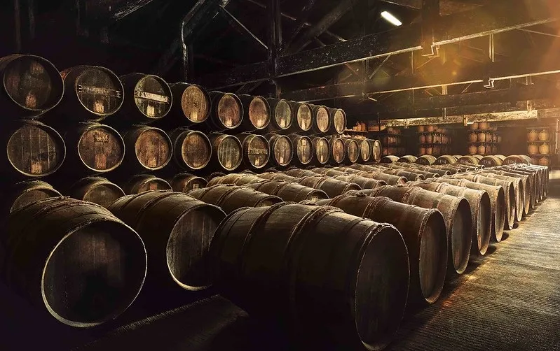 Chai de vieillissement Hennessy à Bordeaux avec des rangées de fûts de chêne empilés en hauteur, éclairage ambré chaleureux mettant en évidence l'atmosphère historique de la cave.