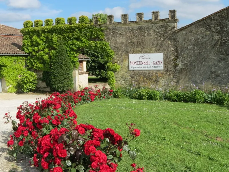 Façade du Château Monconseil-Gazin à Bordeaux avec ses murs en pierre, créneaux, lierre vert et rosiers rouges en premier plan
