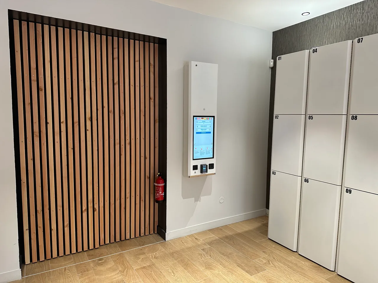 Intérieur d'une consigne automatique Popin Locker à Bordeaux avec casiers blancs numérotés, borne interactive de collecte, porte à lames de bois et extincteur
