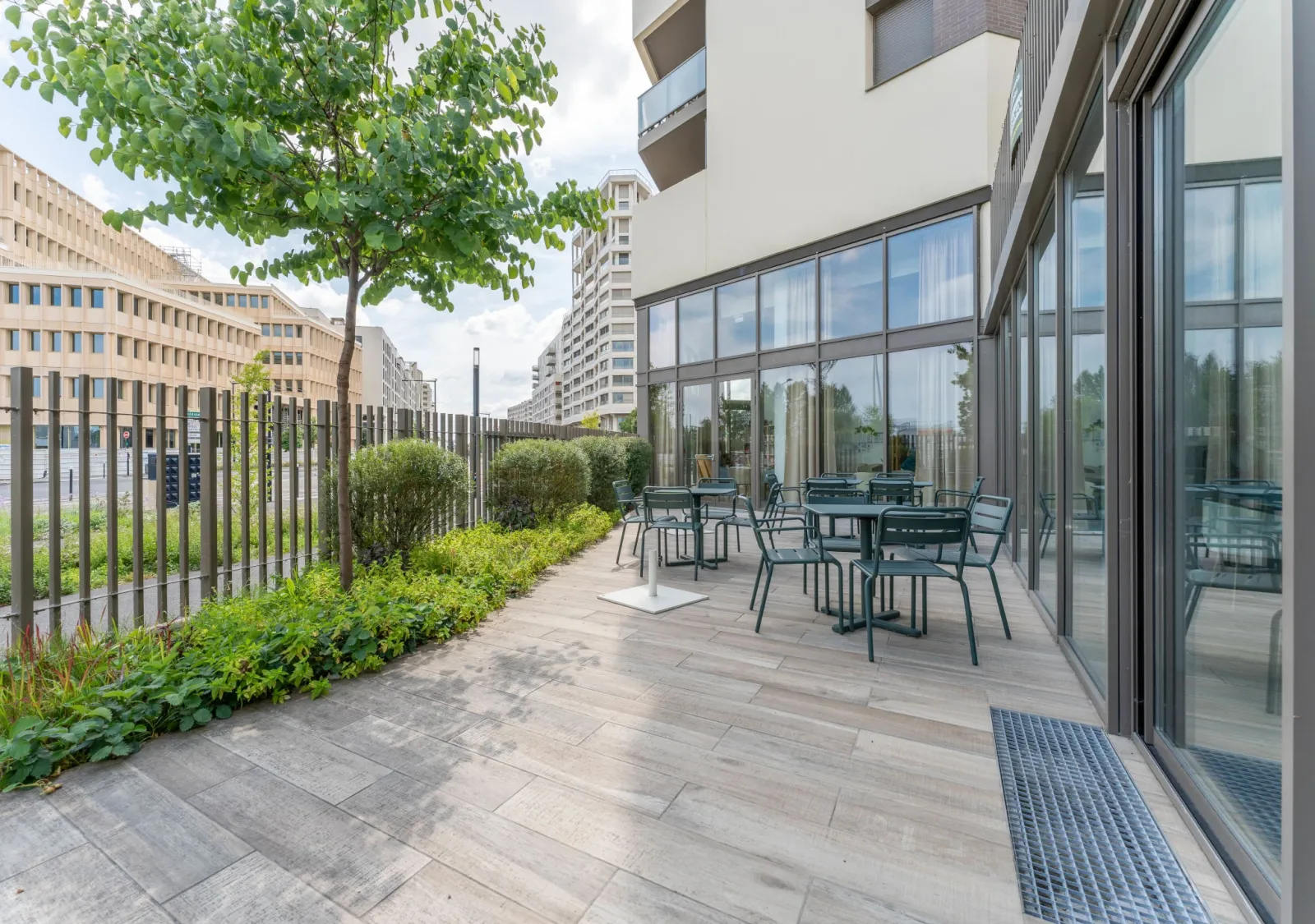 Terrasse moderne d'une résidence seniors avec mobilier de détente, vue sur jardins paysagés et immeuble environnant à Bordeaux.