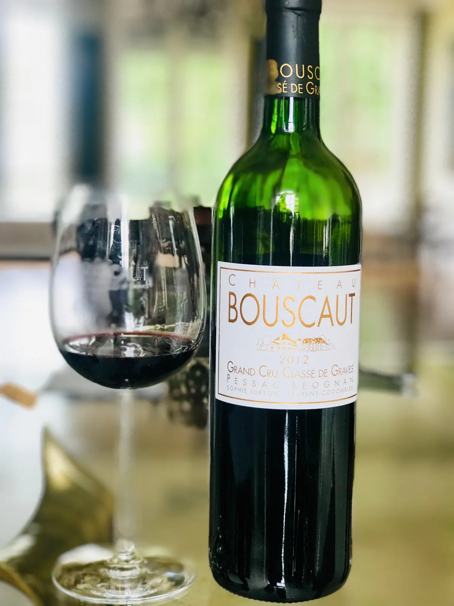 Bouteille de Château Bouscaut, vin rouge de Bordeaux Grand Cru Classé de Graves, avec un verre rempli en arrière-plan