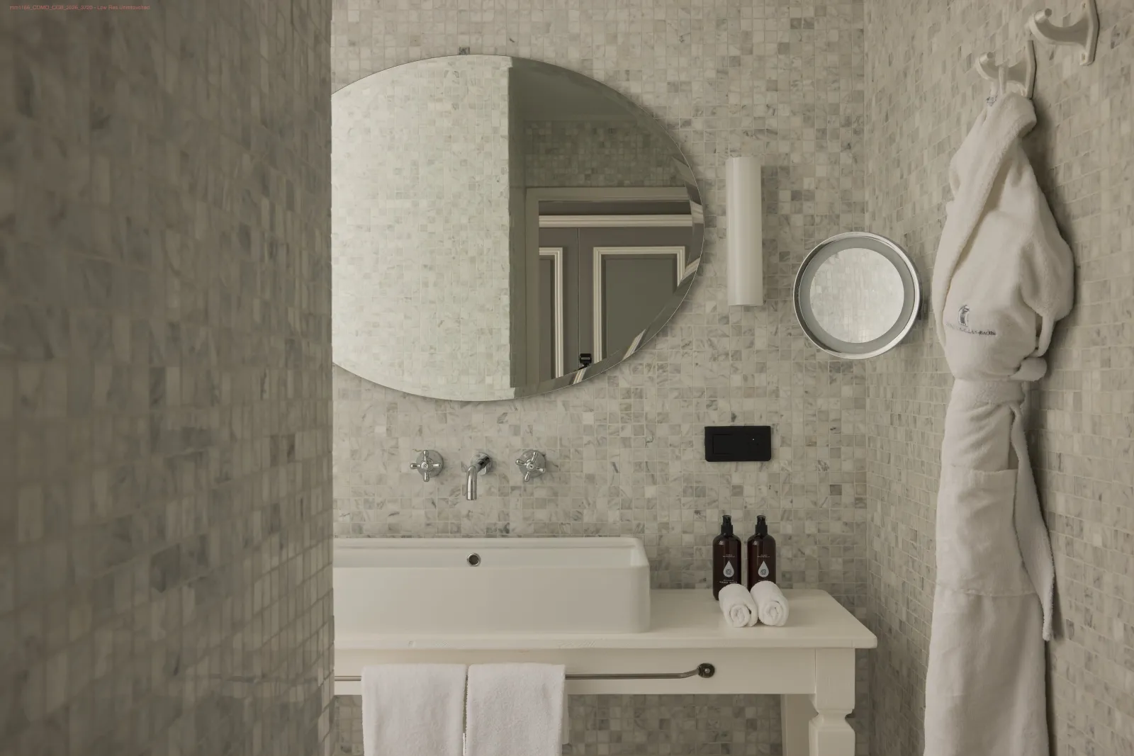 Salle de bain élégante avec carrelage beige, vasque blanche rectangulaire, deux miroirs ronds et ovales, robinetterie chrome, serviettes blanches et produits de toilette, dans un style minimaliste épuré.