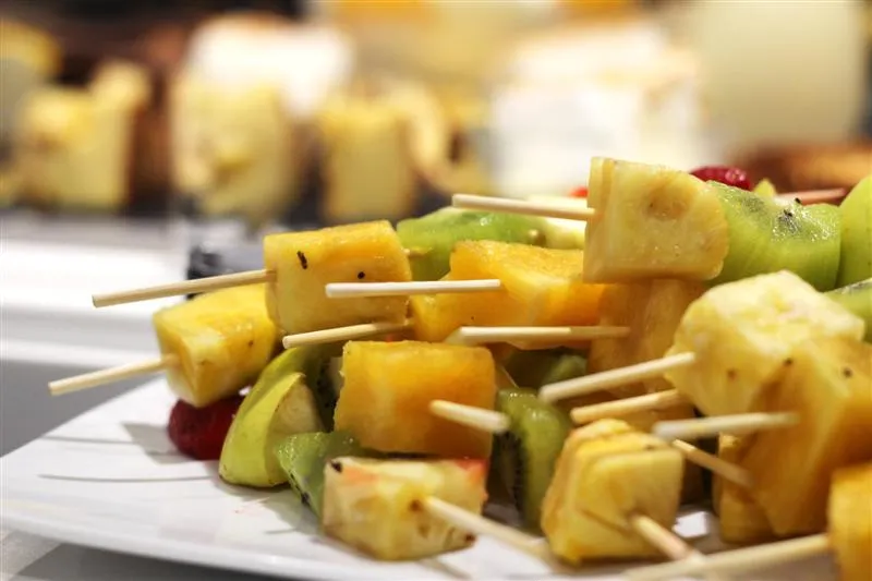 Brochettes de fruits exotiques grillées composées d'ananas et de kiwi sur des piques en bois, disposées sur une assiette blanche