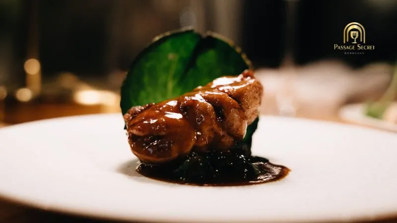 Plat gastronomique du restaurant Passage Secret à Bordeaux : foie gras poêlé garni de feuilles de menthe fraîche, présenté sur une assiette blanche avec un coulis noir