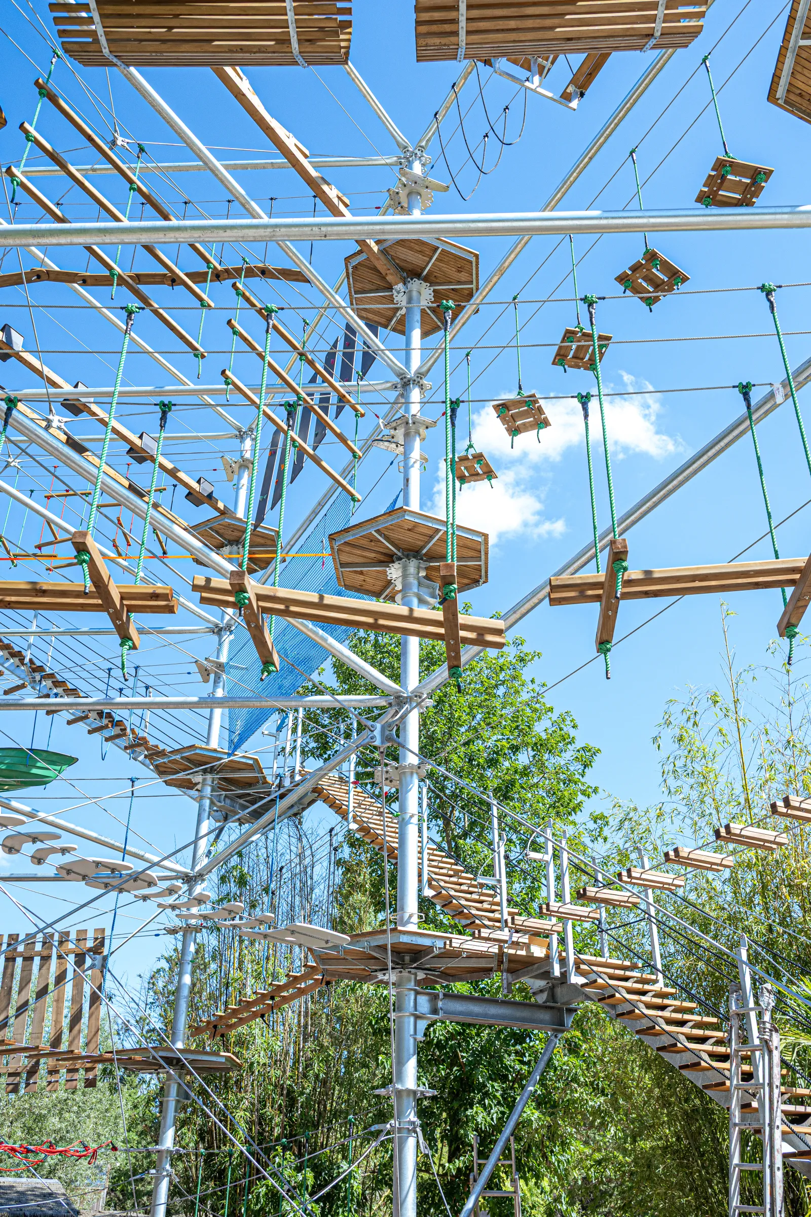 Parc d'aventure Les Cimes de Bordeaux à Pessac avec parcours suspendu dans les arbres, ponts de cordes, poutres en bois et filets de sécurité sous un ciel bleu.