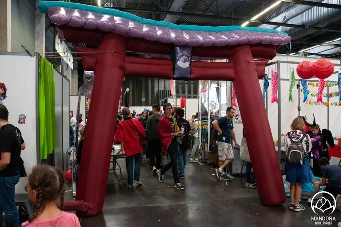 Entrée en forme de portique torii rouge au festival Animasia de Bordeaux, avec des visiteurs passant sous la structure décorée de lanternes, dans un hall d'exposition.