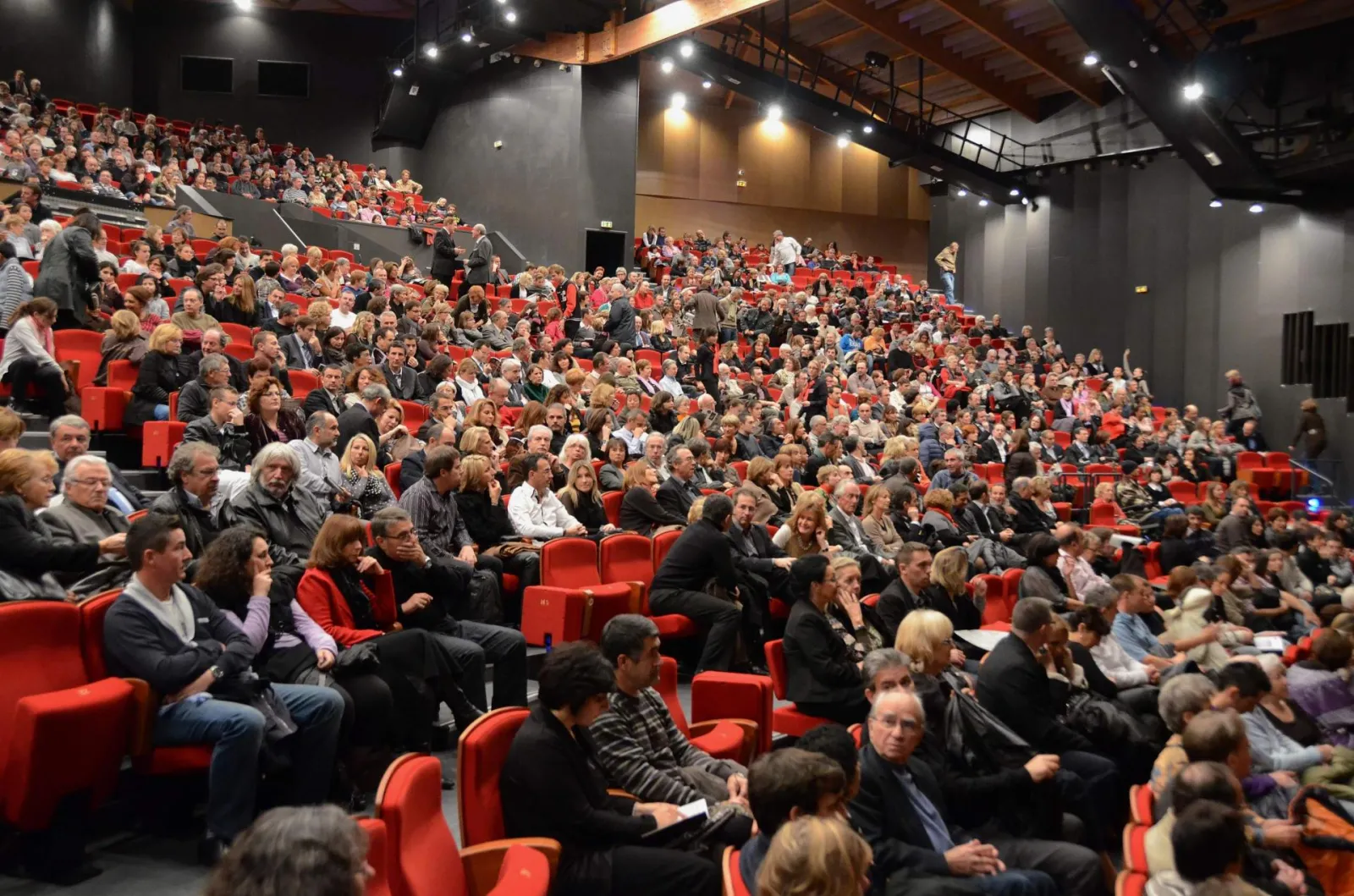 Vue d'une salle de cinéma remplie de spectateurs assis dans des fauteuils rouges, avec des rangées de sièges s'étendant vers l'écran.