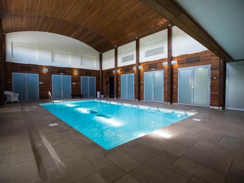 Piscine intérieure moderne aux Les Bains de Margaux à Bordeaux, avec eau turquoise, vestiaires en bois clair, plafond arrondi et éclairage naturel