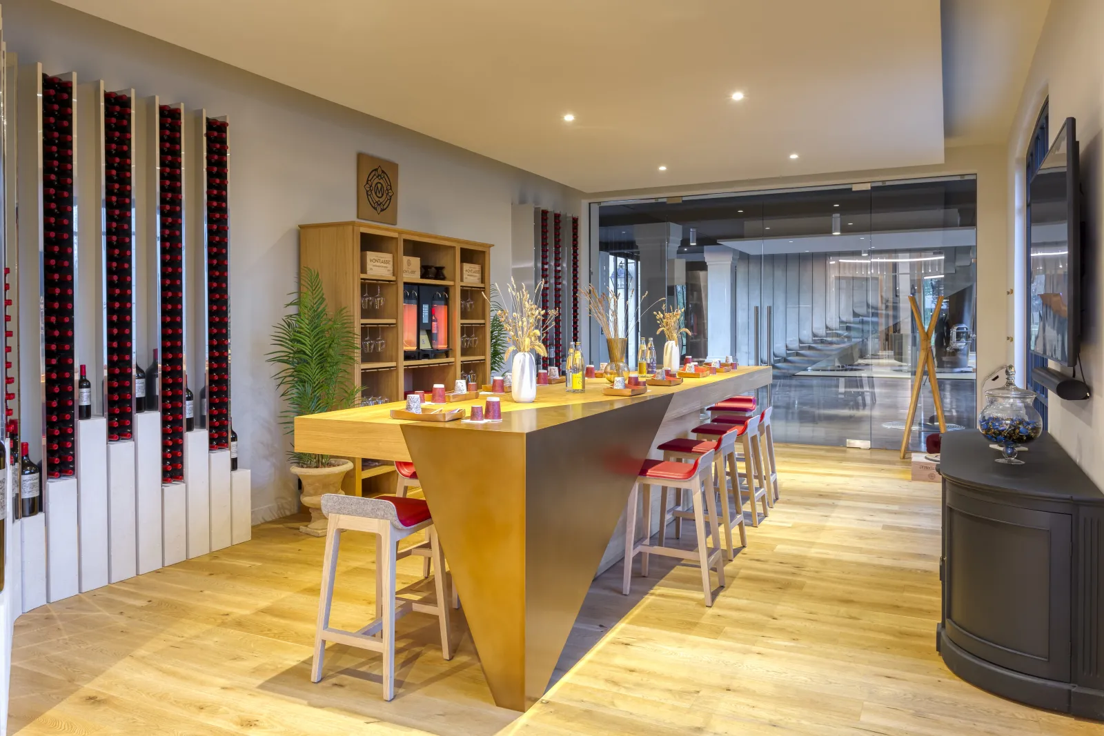 Intérieur moderne d'une cave à vin avec un comptoir jaune vif, des tabourets rouges, des rangements de bouteilles en display mural, et des étagères en bois au Château Montlabert à Bordeaux