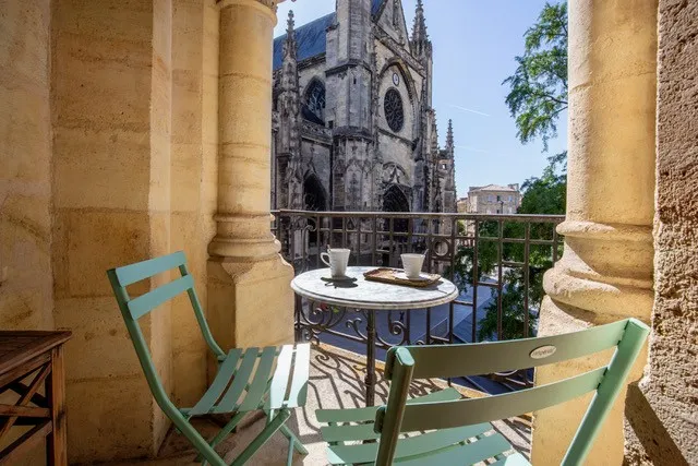Terrasse avec chaises vertes surplombant la Basilique Saint-Michel de Bordeaux, entourée de colonnes en pierre dorée