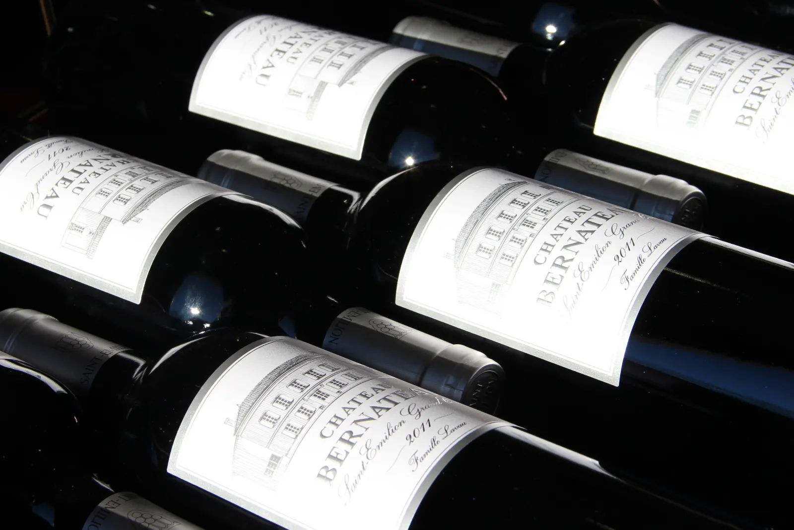 Bouteilles de vin rouge du Château Bernateau de Bordeaux alignées dans un casier de rangement, avec des étiquettes blanches visibles.