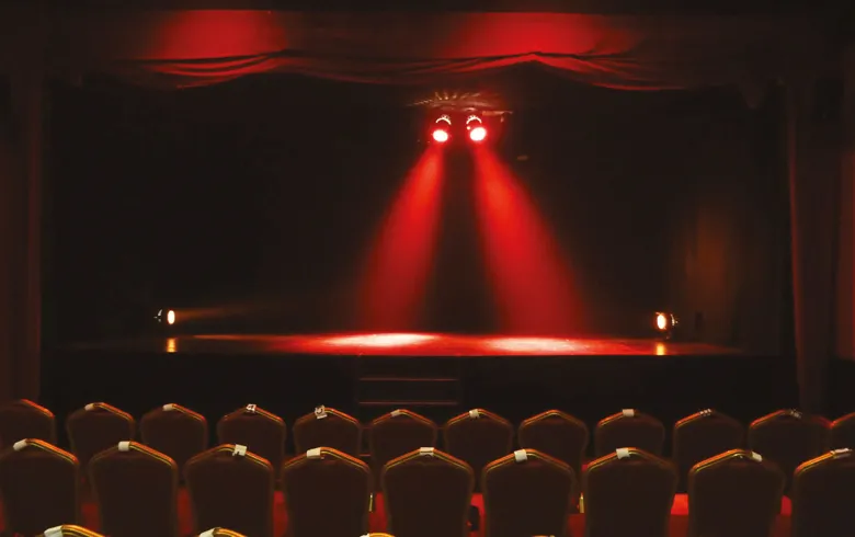 Scène du Théâtre des Chartrons à Bordeaux illuminée par des projecteurs rouges, avec des rangées de sièges en velours bordeaux au premier plan