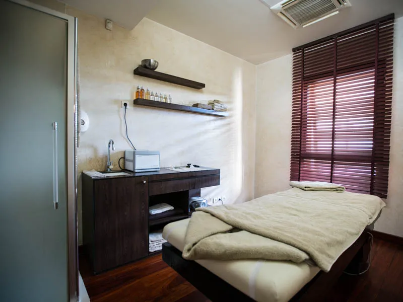 Chambre spa minimaliste avec lit double, bureau en bois foncé, étagères murales, stores bordeaux et sols en parquet, à Les Bains de Margaux à Bordeaux