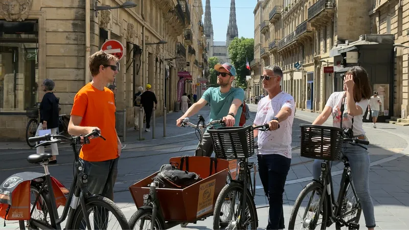 Groupe de touristes à vélo dans une rue piétonne de Bordeaux, avec des vélos de location et une vue sur une église en arrière-plan