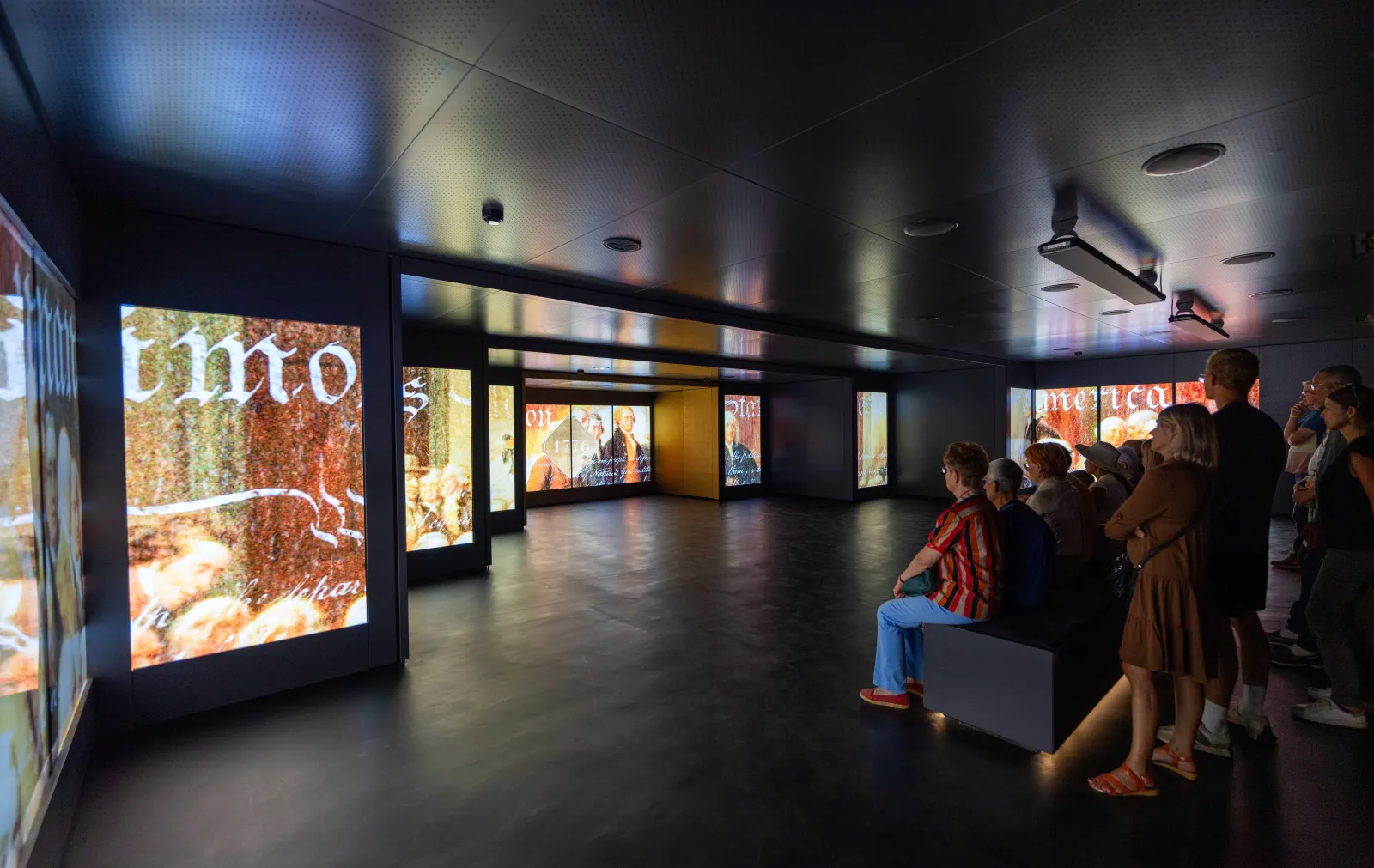 Visite interactive à la Maison Hennessy de Bordeaux : groupe de visiteurs observant des écrans numériques affichant l'histoire et l'héritage de la cognac dans un espace moderne aux murs noirs et plafond éclairé.