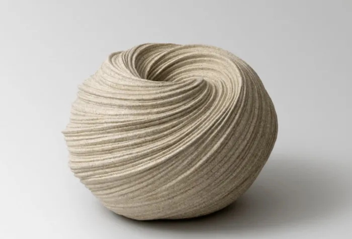 Sculpture céramique de forme sphérique avec des lignes ondulantes gravées, de couleur beige clair, présentée sur fond blanc
