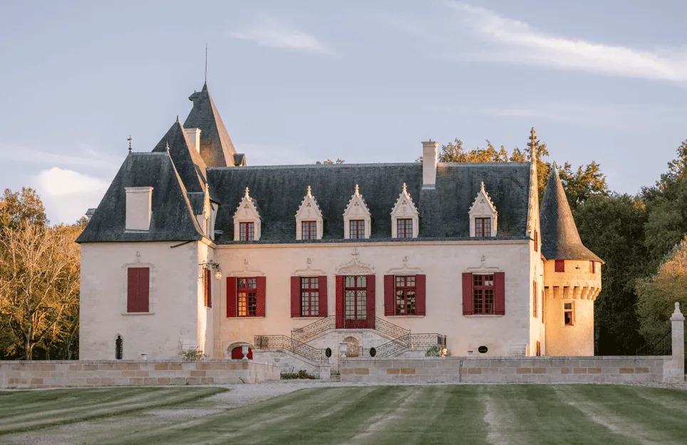 Château Olivier à Bordeaux, un édifice blanc avec toits ardoisés pointus, fenêtres rouges et tours d'angle, entouré d'un parc avec pelouse tondue.