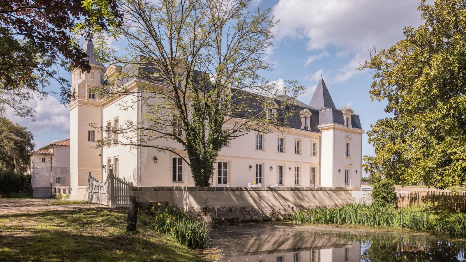 Château Sénéjac à Bordeaux, élégante demeure du XIXe siècle avec tours pointues, façade blanche et rose, entouré d'arbres, avec un petit pont enjambant un étang en premier plan