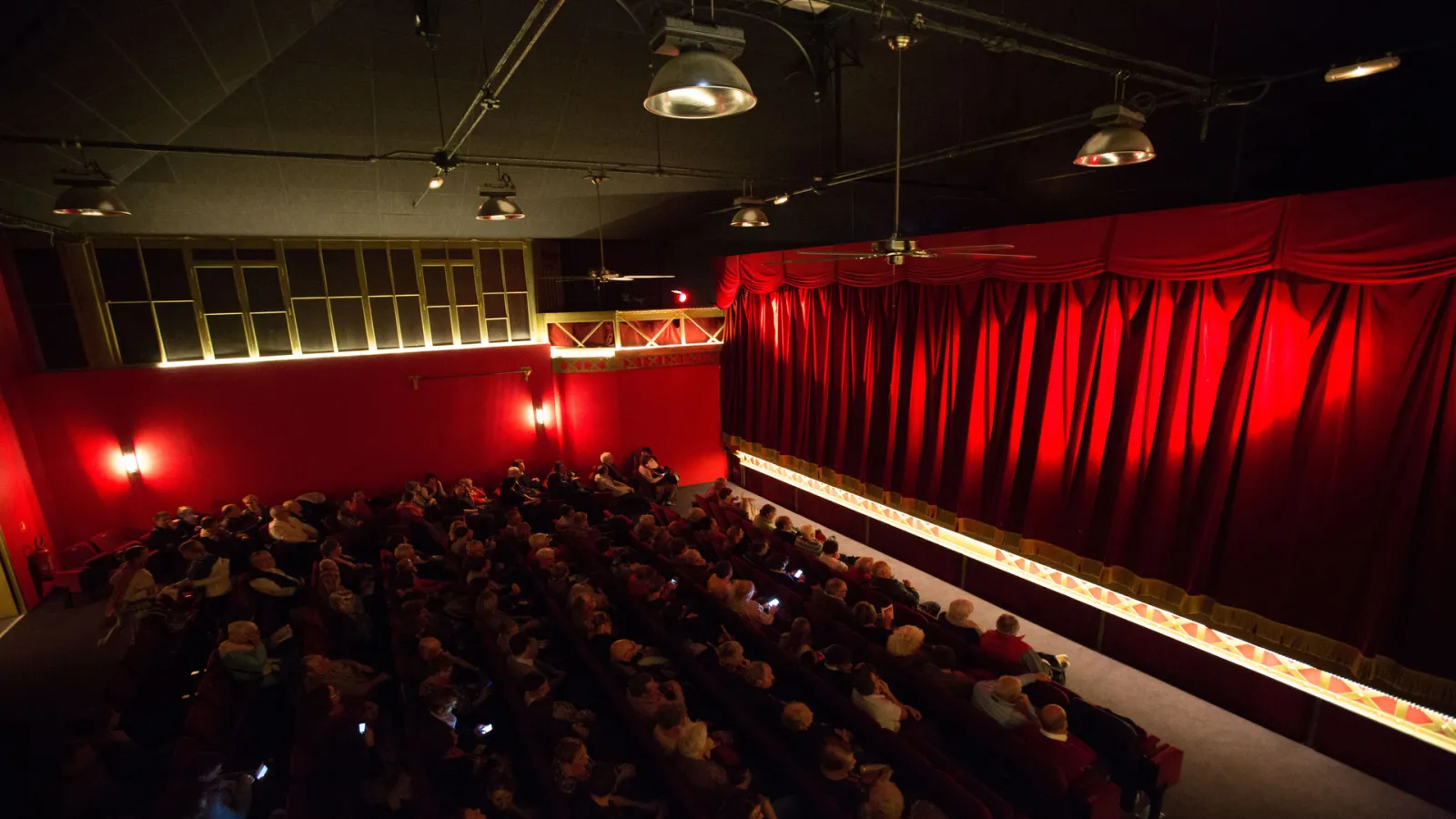 Intérieur du Théâtre des Salinières à Bordeaux avec une salle remplie de spectateurs assis face à la scène encadrée de rideaux rouges.