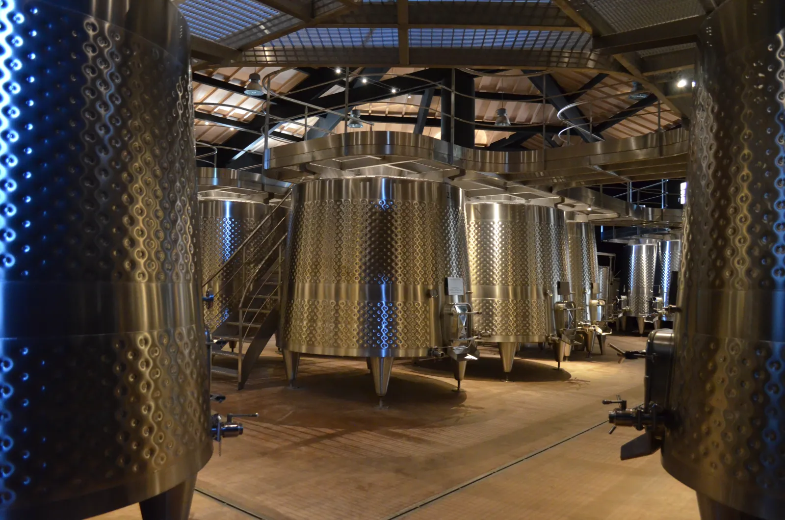 Intérieur d'une cave de vinification moderne avec des cuves en acier inoxydable cylindriques alignées dans un hangar lumineux, éclairé par des néons bleus, à Bordeaux.