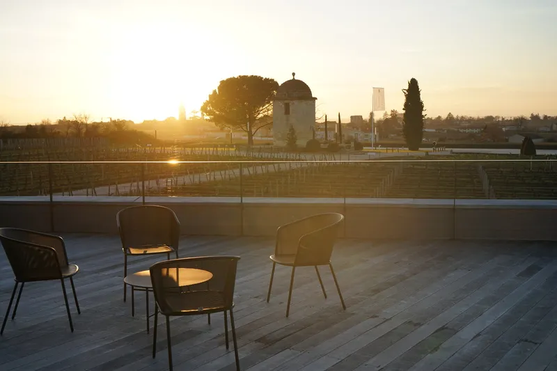 Terrasse avec trois chaises modernes face aux vignobles du Château Balestard La Tonnelle au coucher de soleil, Bordeaux