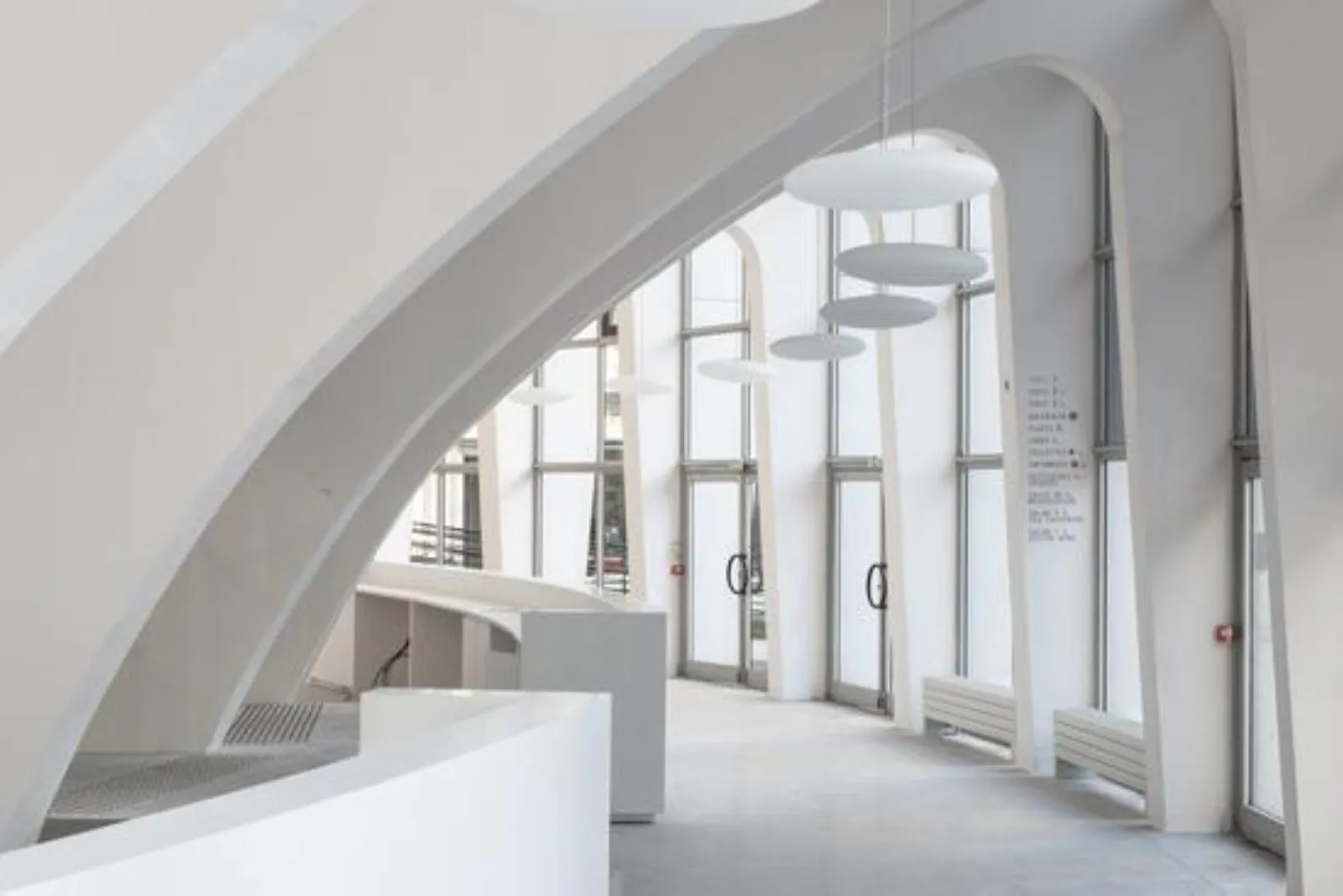 Intérieur moderne du Palais des Sports de Bordeaux avec architecture épurée, grandes baies vitrées, plafond arrondi blanc et luminaires suspendus.