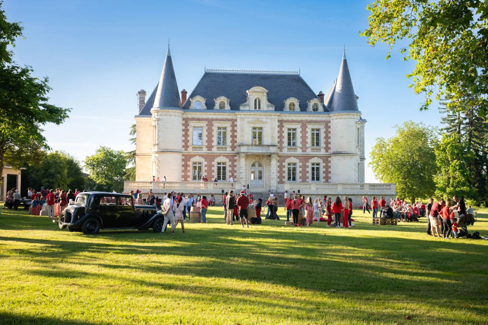 Château Lamothe Bergeron à Bordeaux : imposant château blanc et rose avec tourelles pointues, entouré d'une pelouse verte où se rassemblent des visiteurs et une voiture ancienne.