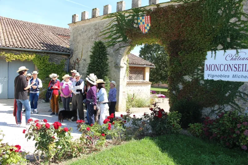 Un groupe de visiteurs en visite guidée devant l'entrée du Château Monconseil-Gazin à Bordeaux, avec ses murs historiques couverts de lierre et ses fleurs rouges en premier plan.