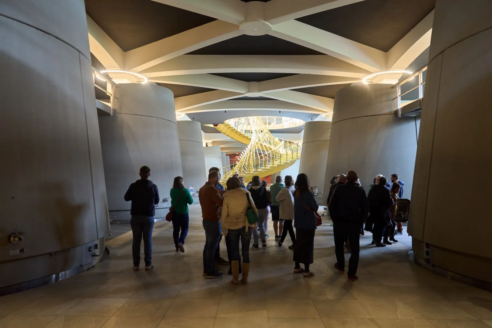 Groupe de visiteurs dans un espace moderne avec plafond géométrique illuminé et vue sur un escalier jaune en arrière-plan, au Château Plain Point de Bordeaux.