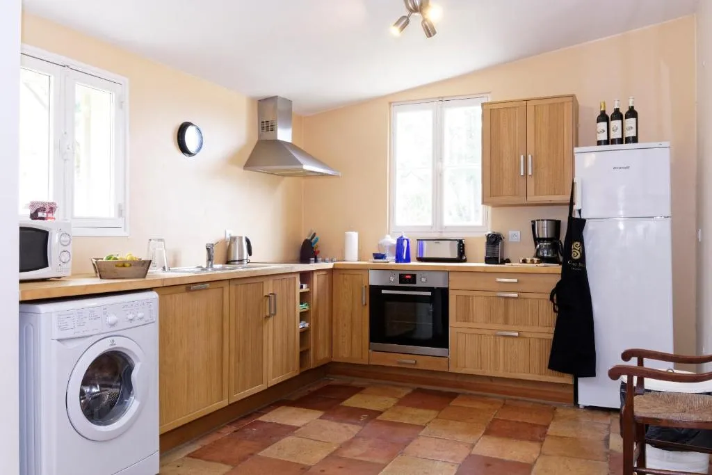 Cuisine moderne avec meubles en bois, électroménagers blancs, carrelage en terre cuite, murs jaune pâle et fenêtres lumineuses