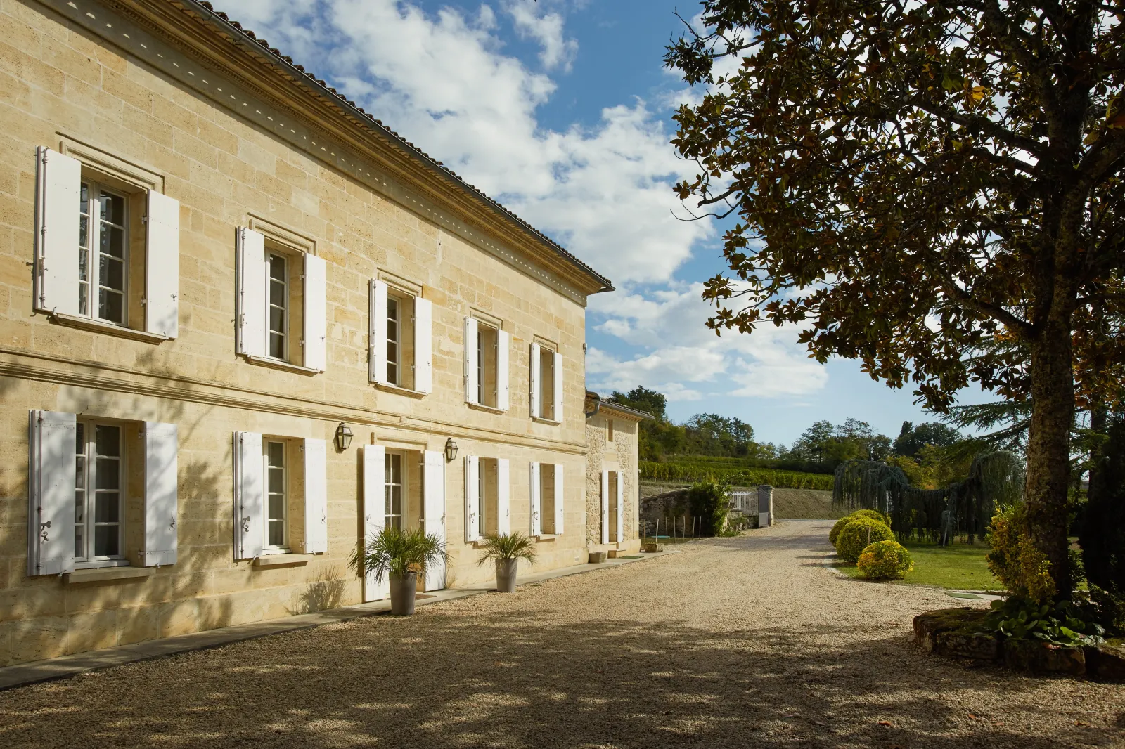 Façade du Château Bernateau à Bordeaux, bâtisse en pierre de taille avec volets blancs, cour de gravier et parc arborisé en arrière-plan.