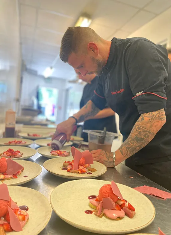 Un chef cuisinier prépare des assiettes de homard au Bistrot du Lac à Bordeaux, en dressant les fruits de mer sur des assiettes blanches avec précision.