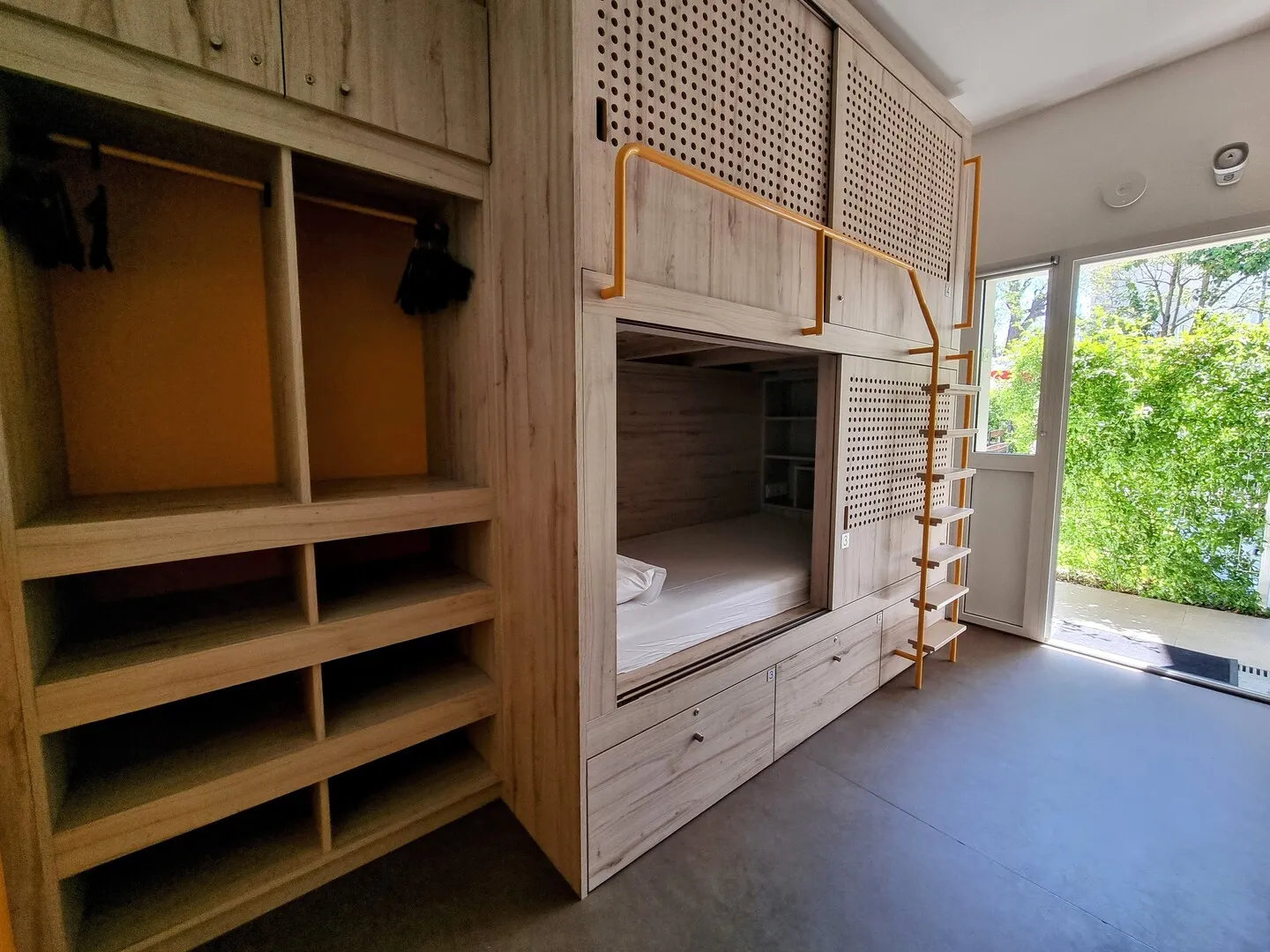 Chambre moderne d'un auberge à Bordeaux avec lits superposés en bois, étagères de rangement, et vue sur la verdure par les fenêtres