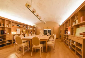 Salle de dégustation élégante du Chapon Fin à Bordeaux avec table en bois, chaises rembourrées beiges, étagères en bois clair remplies de décoration et de livres, plafond voûté et luminaires modernes.