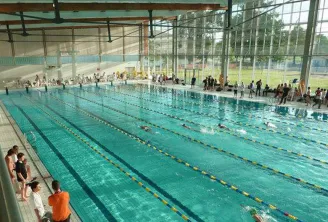 Vue intérieure de la piscine olympique de Villenave d'Ornon à Bordeaux avec plusieurs nageurs dans les couloirs de nage et spectateurs sur les gradins.