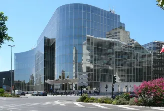 La Bibliothèque municipale Mériadeck de Bordeaux, bâtiment moderne aux façades de verre incurvées, avec des éléments architecturaux en béton, entouré de verdure et de fleurs roses