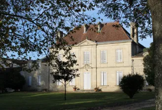 Château Mangot à Bordeaux, une élégante demeure en pierre de taille de couleur crème avec toit en tuiles rouges, entourée d'une pelouse et d'arbres, façade symétrique avec fenêtres blanches et porche central.