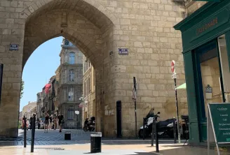 Vue de la rue de Cheverus à Bordeaux sous une arche de pierre, avec la façade verte du café Cassonade et des bâtiments haussmanniens en arrière-plan.