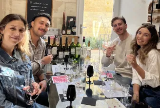 Quatre jeunes adultes souriants lors d'une dégustation de vins à Bordeaux, assis autour d'une table avec plusieurs bouteilles et verres de vin.