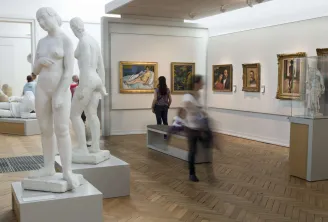 Galerie d'art moderne à Bordeaux avec sculptures blanches au premier plan et portraits peints dans des cadres dorés accrochés aux murs, visiteurs parcourant l'exposition.