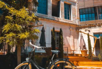 Vélo noir garé devant un bâtiment en briques rouges avec façade moderne à Bordeaux, sous un ciel bleu dégagé avec arbres aux feuillages jaunes.