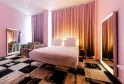 Chambre moderne de l'hôtel Mama Shelter à Bordeaux avec murs roses, lit blanc central, miroirs illuminés, fauteuils à rayures zèbre, rideaux dégradés orange et noir, et tapis géométrique noir et beige.