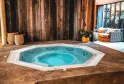 Un jacuzzi turquoise avec jets de massage intégrés, situé dans un espace spa au design moderne avec murs en bois sombre et baies vitrées donnant sur un jardin.