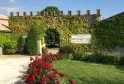 Entrée du Château Monconseil-Gazin à Bordeaux, avec ses murs de pierre couverts de lierre vert, un panneau d'identification, des roses rouges en première ligne et un jardin paysagé.