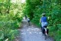 Cyclistes et piétons sur un chemin ombragé bordé de végétation luxuriante dans le Bois du Déhès à Bordeaux