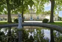 Vue du Château Siran à Bordeaux avec un bassin réfléchissant au premier plan, une statue en pierre, de grands arbres centenaires, et le bâtiment principal en pierre de taille en arrière-plan.