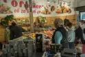 Clients dans une boutique de fruits et légumes frais du marché couvert des Chartrons à Bordeaux, avec des étals de produits colorés et des affiches promotionnelles.
