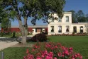 Vue du château Luchey-Halde à Bordeaux avec ses bâtiments en pierre blanche et rouge, entourés d'un parc verdoyant orné de fleurs roses et d'un grand arbre.